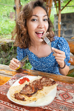 A woman with an appetite eats a delicious barbecue or fried meat in a restaurant on the terrace