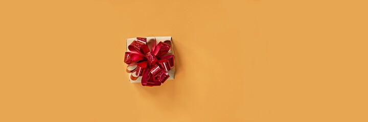 Banner with a Gift box, with a bright shiny red bow on a bright orange (yellow) background. Present for birthday, christmas, new year. Festive concept.