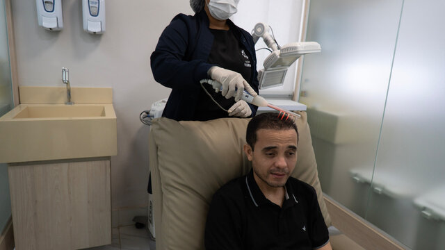 woman doing laser therapy on man's hair in medical clinic on front