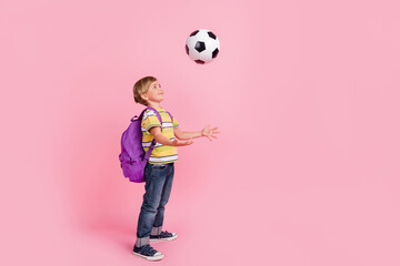 Full length photo of young small happy boy throw ball wear bag smile isolated on pink color background