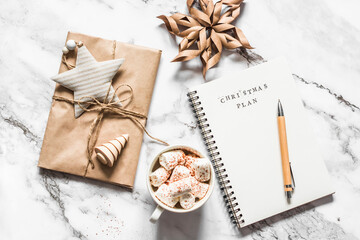 Obraz na płótnie Canvas Christmas background - blank notepad with christmas plans, gift box, cup of hot chocolate on a light background, top view