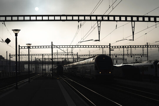 Brouillard dans la gare de Romont en Suisse, photo en contre jour avec les voies et les poteaux.