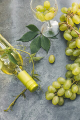 Top view of bottle white wine, green vine, wineglass and ripe grape on vintage gray stone table...