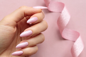 Female hand with a light pink long nails on a light pink background decorated by pink ribbon