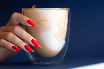 Girl`s hand with a beautiful red manicured nails and glass of coffee on the blue background