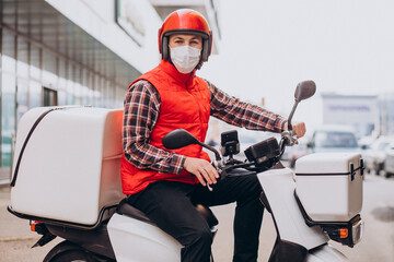 Food delivery boy driving scooter with box with food and wearing mask