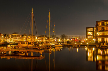 Fototapeta na wymiar Haarlem, The Netherlands, November 19, 2021: night view of the river Spaarne, with a jetty and sailboats next to a new residential neighbourhood