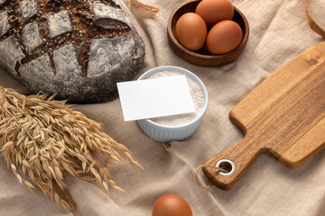 Fototapeta na wymiar Blank business card, fabric background with bread, eggs, flour, serving board, bakery branding mockup, empty space to display your logo or design.