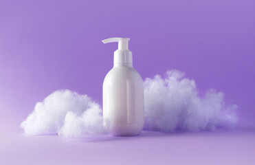 Lotion with fluffy clouds on violet background. Cosmetic white plastic bottle with pump beauty product for skincare or body care. Concept care with sensitive skin. Creative still-life photo