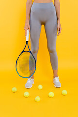 partial view of sportswoman in grey leggings holding racquet while standing near tennis balls on yellow