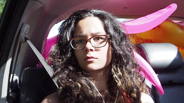 Portrait of a teenage brunette girl in glasses with headphones riding on the passenger seat of a car and looking bored out the window.