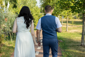 Fototapeta na wymiar The newlyweds walk along the park path holding hands.