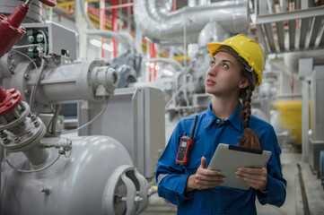 Female engineer smiling with yellow hard hat helmet and holding tablet working inside factory