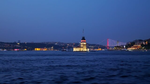 Maiden's Tower seen from sailing ship, illuminated Bosphorus bridge on background. Late evening time at Istanbul city, charming view in twilight, dark blue color of water and sky