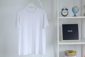 Mockup of white t-shirt hanging on metal hanger with decorations on iron rack isolated on white...