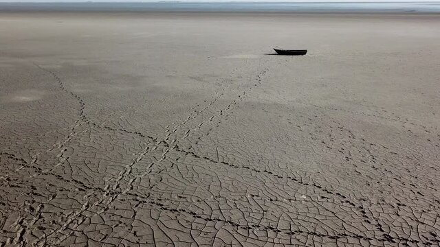 Top view of boat at shore of dried up sea, global warming and drought concept. Windy weather desert landscape with human and animal tracks on dry clay. 4k high quality cinematic drone ungraded footage