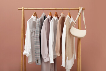 Rack with different stylish clothes and bag on pale pink background