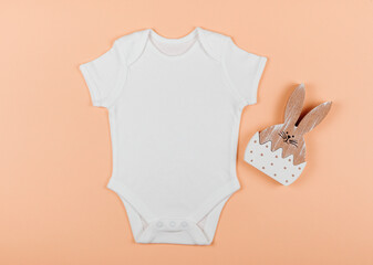 Flat lay of baby cute white bodysuit with wooden toy. Orange background. Baby clothes. Mock up for...