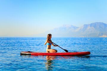 Woman sitting on sup board and enjoying peace and quiet outdoors