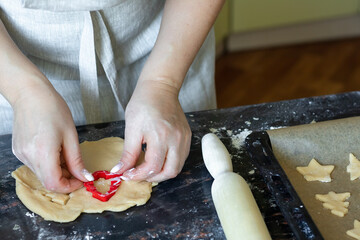 A woman cuts out cookies in the shape of a Christmas tree from the dough, the concept of making Christmas cookies