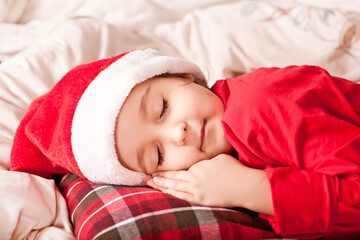 happy child girl in Santa cap waiting Santa and sleep near pine tree on Christmas eve