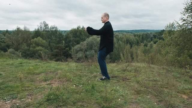 Middle aged Caucasian man practices wushu in the summer in a park on a hill. Traditional Chinese gymnastics qigong and Tai chi. Meditation and relaxation in nature. Healthy lifestyle and sports
