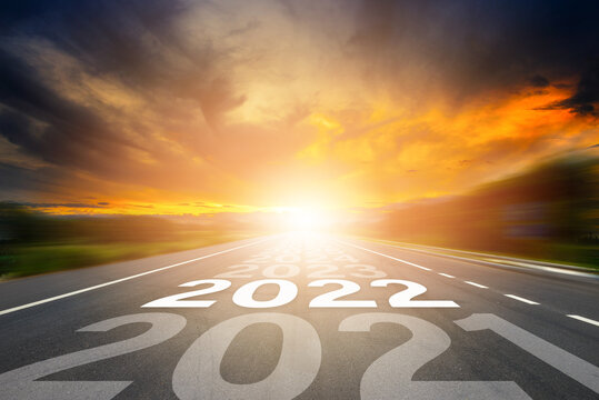 Start to New year 2022 concept. Number of the year written on highway road in the middle of empty asphalt road with sunset or sunrise light above asphalt road.