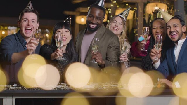 Sliding Shot of Friends Raising Glasses During New Year's Eve Celebrations to Camera