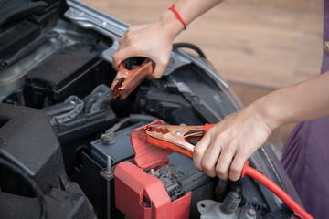 Asian young woman charging a car battery from the other car by using battery connector jump between...