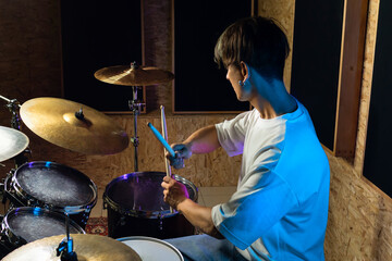 Drummer playing drums at drum kit with colorful backlit on background. Rock musician playing on...