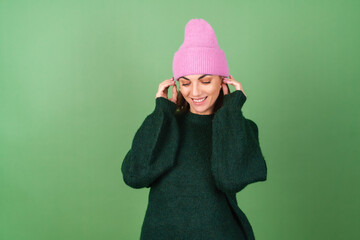 Young woman on a green background in a warm cozy sweater and a pink hat cute smiling