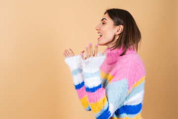 A young woman on a beige background in a bright multi-colored cozy knitted sweater is excited, surprised, shocked