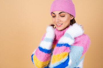 Young woman on a beige background in a bright multi-colored cozy knitted sweater and a hat comfortably hugs herself, warmth and comfort