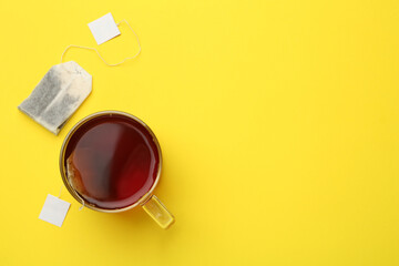 Tea bags and glass cup of hot drink on yellow background, flat lay. Space for text
