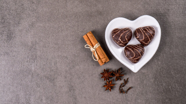 Typical German gingerbread cookies in heart shape on a white heart-shaped plate on a gray background. Traditional Christmas treat. Top view, copy space. - Powered by Adobe