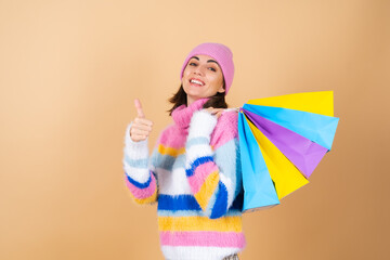 Young woman on a beige background in a bright multi-colored cozy knitted sweater, a plaid skirt holds shopping packages cheerfully posing