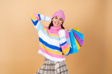 Young woman on a beige background in a bright multi-colored cozy knitted sweater, a plaid skirt holds shopping packages cheerfully posing