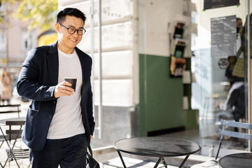 Asian businessman with coffee going from entrance of building. Smiling modern adult successful man...