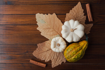Autumn flat lay with yellow gourds, white mini pumpkins, dry maple leaf, cinnamon sticks on wooden rustic background. Copy space for text. Thanksgiving table decorations.