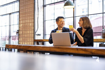 Multiracial friends or business partners talking and drinking beer in modern pub. Concept of rest and leisure. Business deal while drinking at the bar. Pleased young european woman and adult asian man