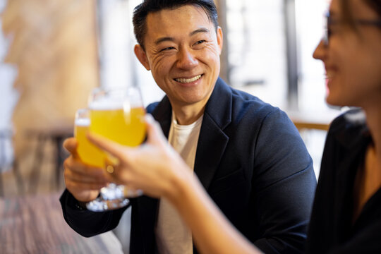 Multiracial Friends Or Business Partners Talking And Drinking Beer In Modern Pub. Concept Of Rest And Leisure. Business Deal While Drinking At The Bar. Pleased Young European Woman And Adult Asian Man