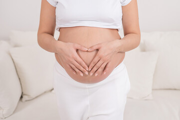 Close-up of a pregnant woman holding her hands in the shape of a heart on her stomach.