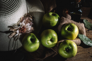 Green apples in sack with hat on rustic wooden table.
