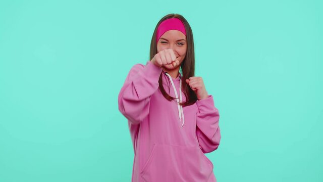 Aggressive angry sincere teen student girl 20s years old in pink hoodie trying to fight at camera, shaking fist, boxing with expression, punishment. Young adult woman isolated on blue background