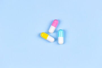 Fototapeta na wymiar Three colorful medicine pills capsules on light blue background. Top view, flat lay, copy space for text