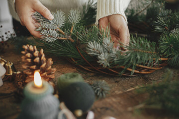 Making rustic christmas wreath close up. Woman hands holding fir branch and arranging christmas...