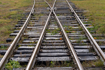 Fototapeta premium Photo of a wooden railway tracks which are merged and green grass. Train and transportation concept