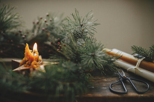 Merry Christmas and Happy holidays. Christmas advent. Stylish burning star candle in christmas wreath with spruce branches and berries on rustic wooden background. Atmospheric moody image