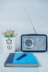 Vintage radio with flower in white vase, a blue book, a pen and sunglasses.