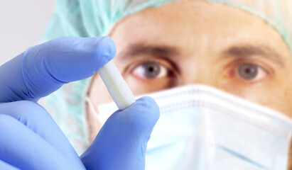 Scientist with medical mask showing white pill. Research concept. Selective focus.